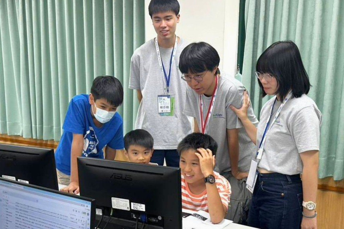 NYCU student volunteers mentor elementary school students during a BeLight AI Semiconductor workshop, guiding them through hands-on activities that introduce programming, AI, and semiconductor concepts in an engaging and accessible way.